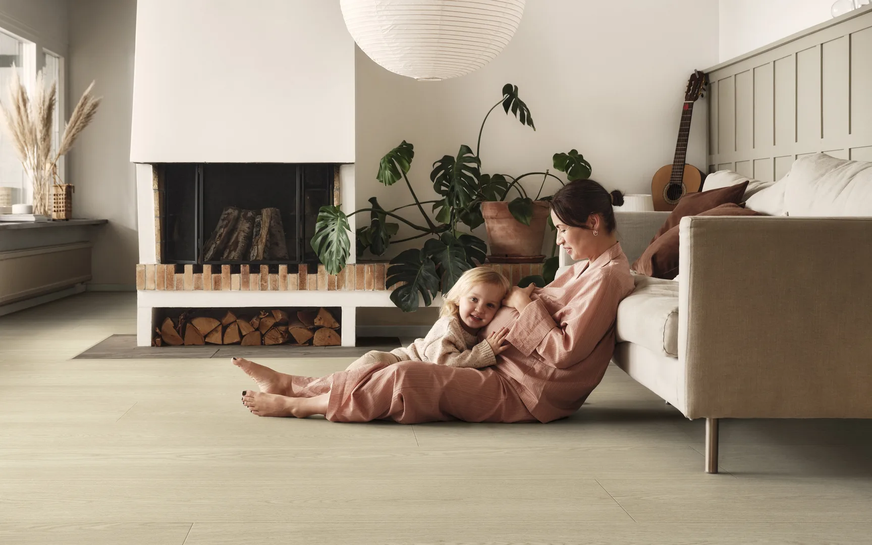 Vrouw met kind op lichte pergo laminaat vloer in de woonkamer met bank en openhaard