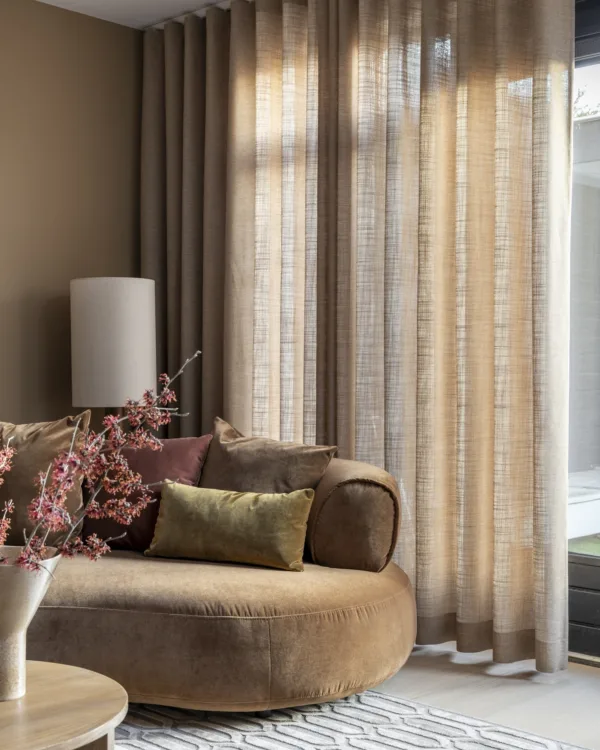 Woonkamer met beige muurverf en ovale bank in dezelfde kleur en bijpassende kamerhoge gordijnen