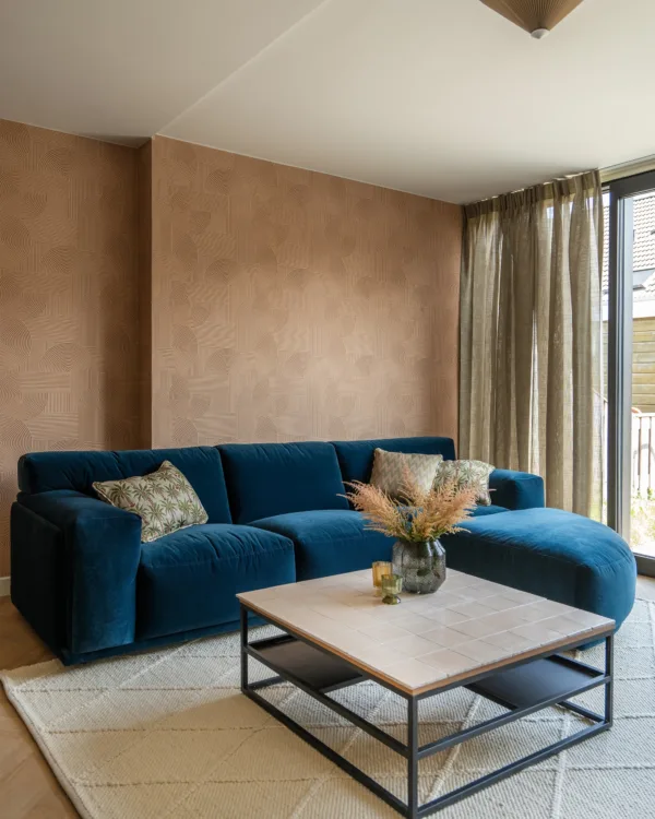 Woonkamer met behangpapier in warme kleur en gestoffeerde hoekbank