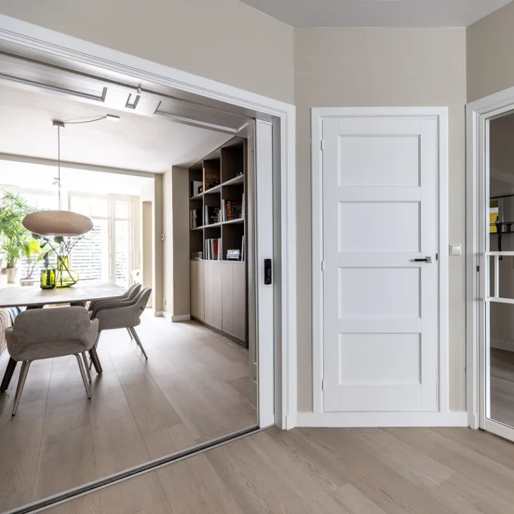 Woonkamer met grote tafel, boekenkast, ensuite deuren en vinylvloer in lichtbruin.