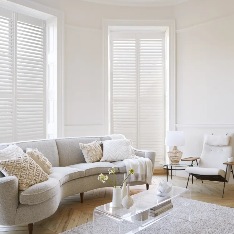 Klassieke woonkamer met houten parket, creme kleurige bank en vloerkleed, hoge ramen met witte shutters