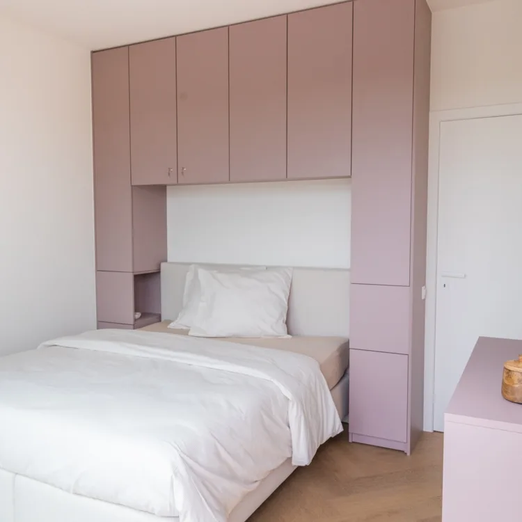Slaapkamer met een lichtroze kast op maat met draaideuren, deurtjes zonder grepen voor een strakke look.